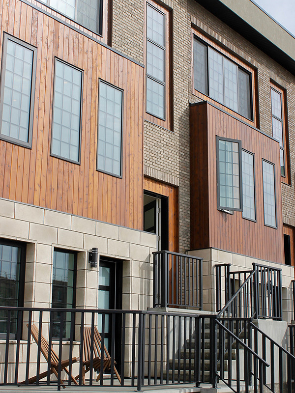 Exterior brownstone townhomes in Calgary's new home development of Greenwich. Greenwich townhomes are 3 storeys and feature black iron balconies with concrete steps.